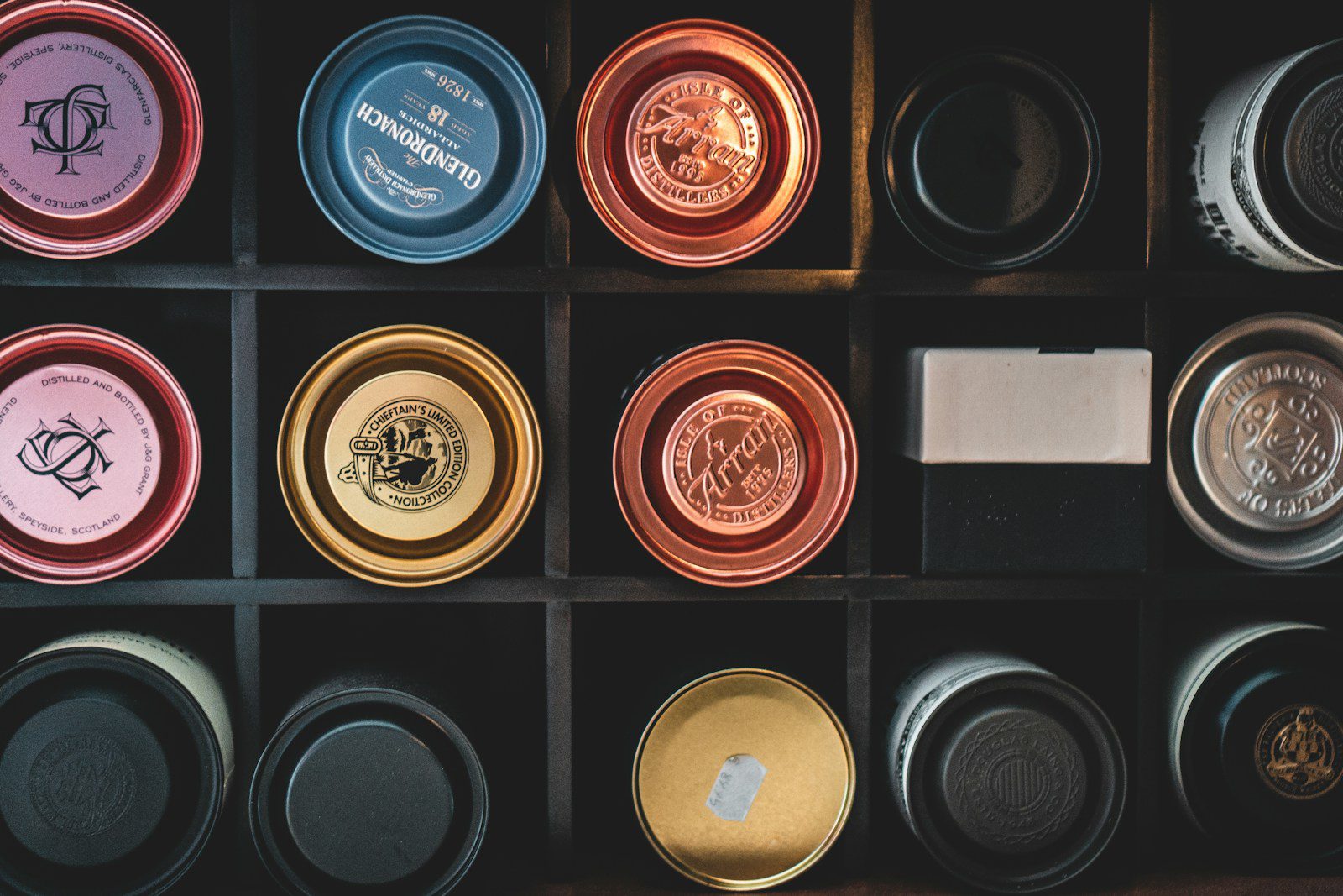 7 Best Whisky Gifts Under $60 That Look Expensive (2026). A top-down grid view of premium whisky tins and boxes, including blue GlenDronach 12, copper and gold Arran Single Malt, and purple Glenfarclas packaging.