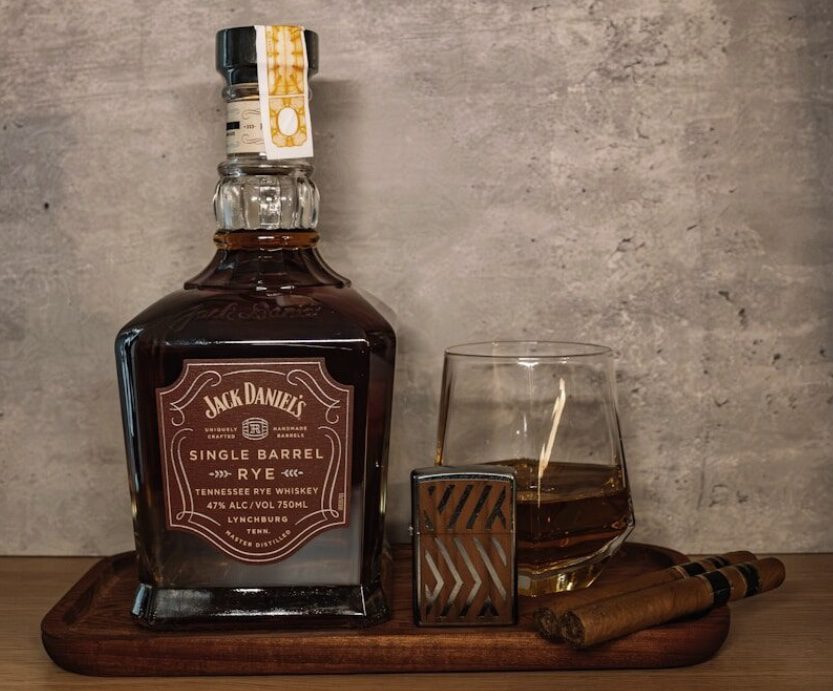 A classic Manhattan cocktail with a cherry garnish next to a bottle of rye whisky